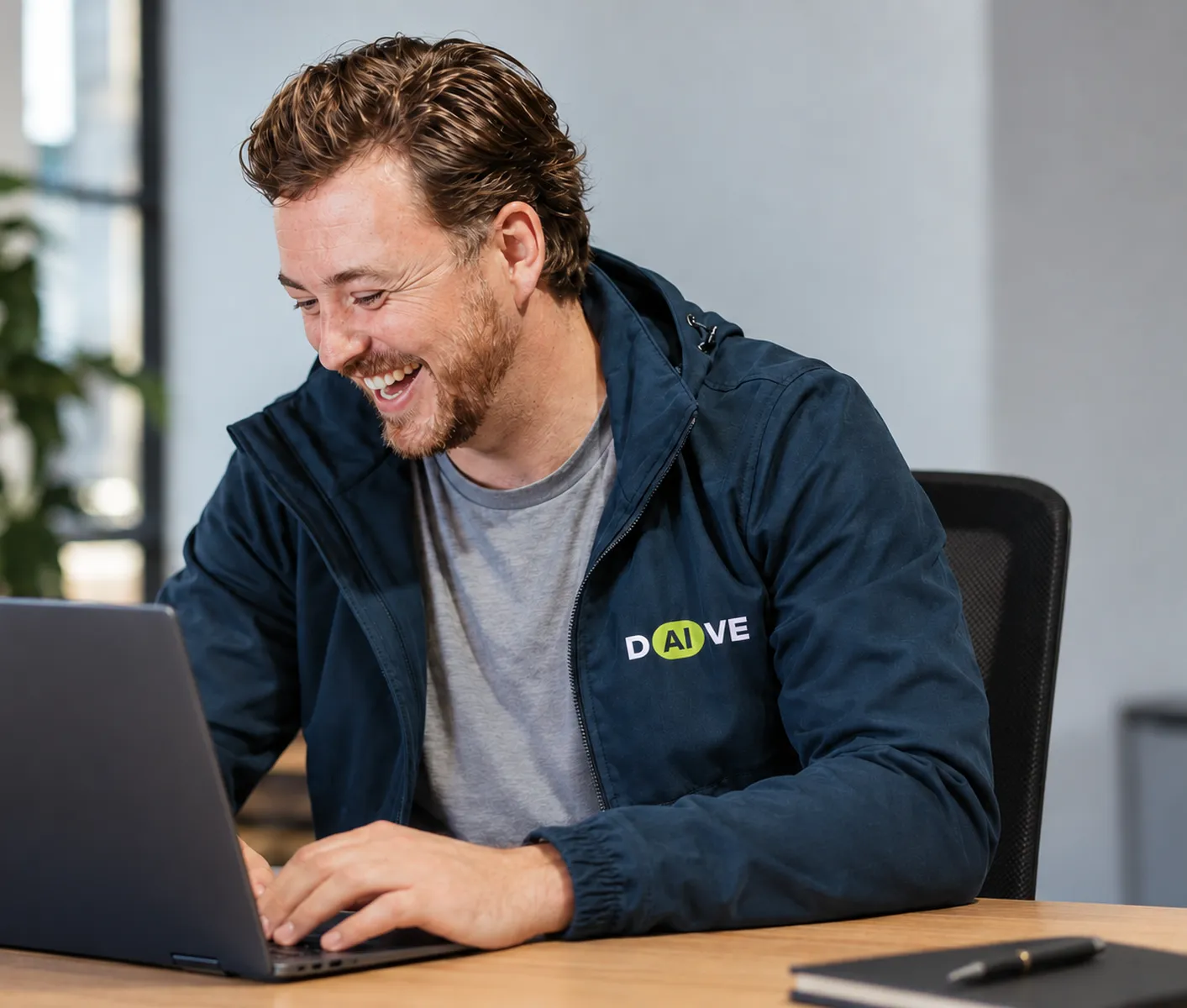 Davey lacht achter zijn laptop, met het DAIVE-logo op zijn jas